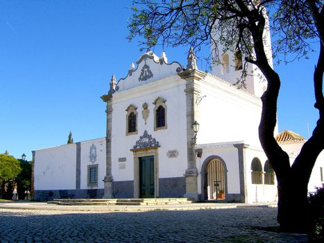 Small church located on Faro, Portugal, with a tree on the right.