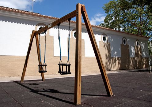 View of a public park with a pair of empty playground swingers.