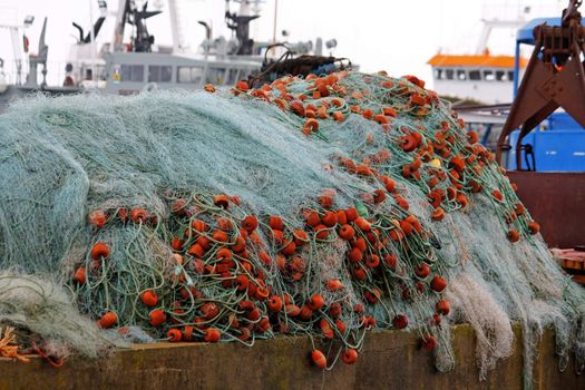 View of a pile of fishing net with plastic floaters, with boats on the background.