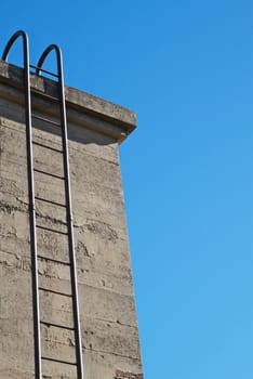 Steel ladder up concrete wall with blue sky background