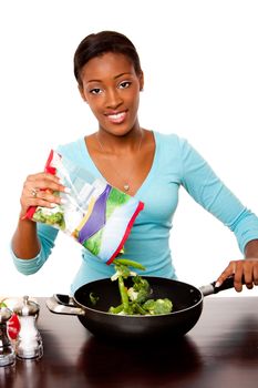 Beautiful happy health conscious young preparing vegetables in pan for stir fry on counter in kitchen, isolated.