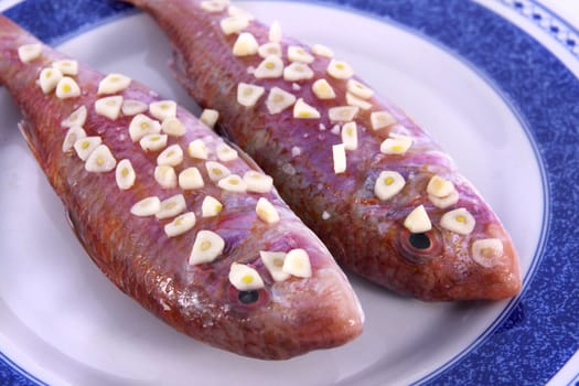 Detail view of two red fish on a plate with garlic on top ready to be made.