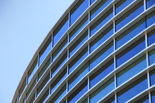 Curved exterior windows of a commercial office building reflecting a blue sky