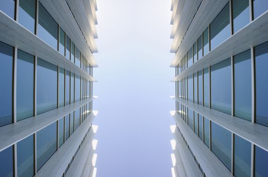 Exterior windows of two identical commercial office buildings looking up from the ground with blue sky reflected in windows