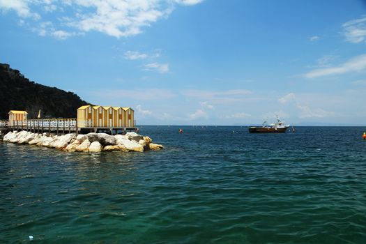 A row of yellow bath houses on a rocky wall next to the water.