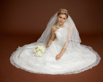 A beautiful young bride in a white dress on a brown background