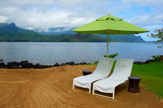 Two white therapy or massage chairs sit under and bright green umbrella on the coast of Kauai, Hawaii
