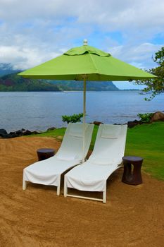 Two white therapy or massage chairs sit under and bright green umbrella on the coast of Kauai, Hawaii