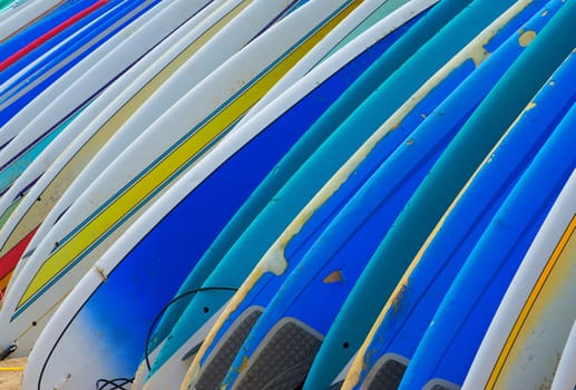 A row of brightly colored rental surf boards with dings and dents from frequent use