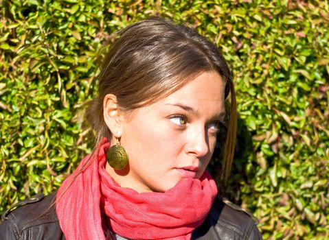 Beautiful girl in a red scarf. Against the backdrop of green hedges. Outdoor portrait.
