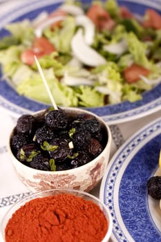 Close up view of a some tempered dry black olives and a salad.