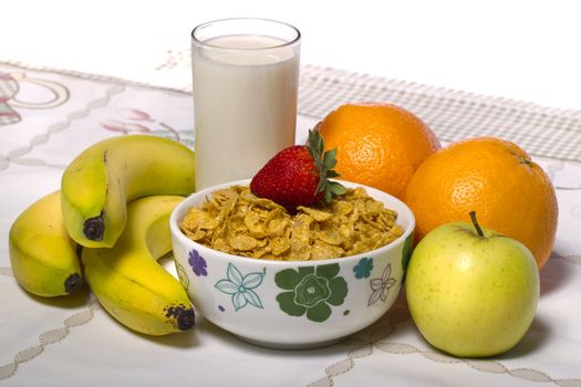 View of a bowl of cereals surrounded by fruit and a glass of milk.