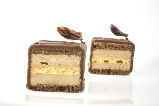 Two petits fours with chocolate frosting, topped with a pecan and isolated on white background.