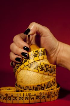 View of a woman's hand grabbing a pear with measuring tape.