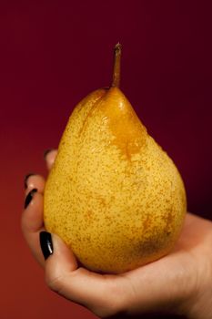 View of a woman's hand holding a wet pear.