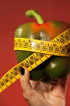 View of a woman's hand holding a bell pepper with measuring tape.
