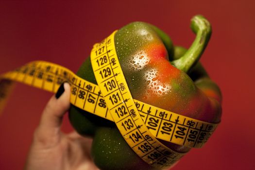 View of a woman's hand holding a bell pepper with measuring tape.