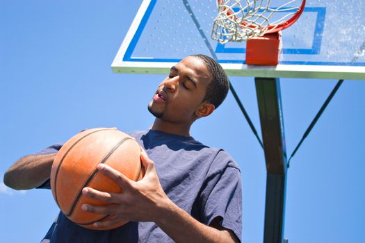 African American man posing with a basketball beneath the backboard.