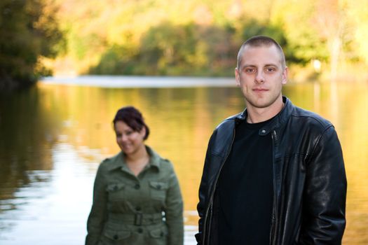 A young happy couple standing by a lake in autumn.  Shallow depth of field with focus on the man in the foreground.