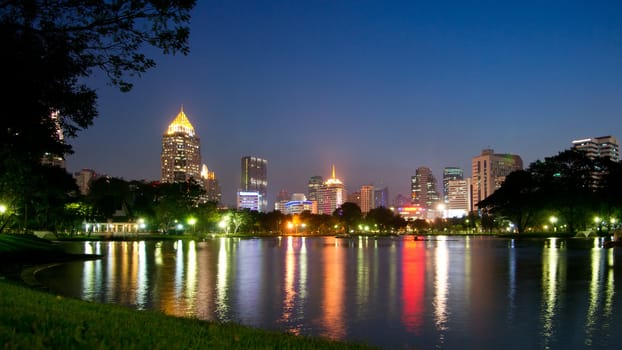 Water reflection of illuminated buildings in Lumphini park, Bangkok, Thailand