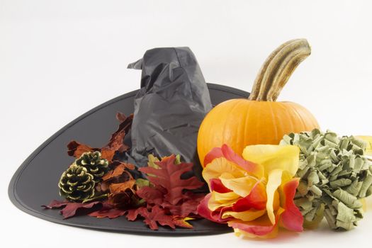 Black witch's hat with objects of the witchly season; hat, pumpkin, flowers, leaves, pine cones.   