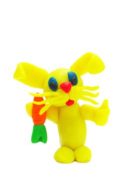 Funny yellow plasticine rabbit with carrot on white background with soft shadows