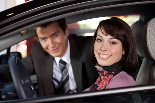 Portrait of young couple sitting in a new car at showroom