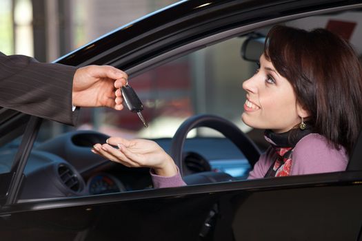 Young woman receiving the car keys from car salesman