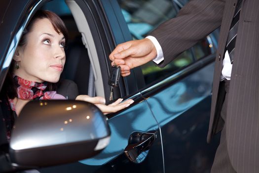 Young woman receiving the car keys from car salesman