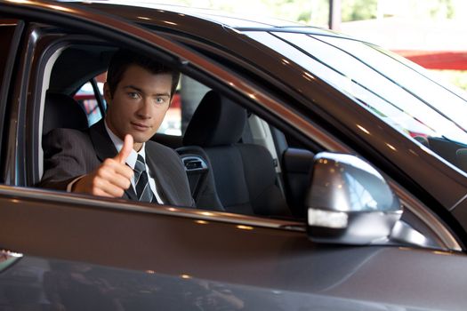 Portrait of man sitting in new car showing thumbs up