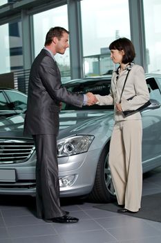 Car salesperson shaking hands with customer at showroom
