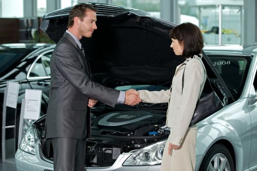 Car salesperson shaking hands with customer at showroom
