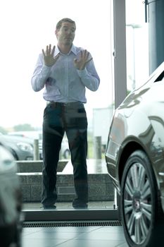 Young man curiously looking at new car in showroom
