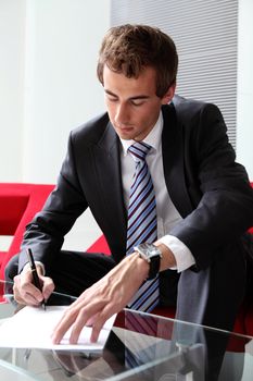 young caucasian businessman sitting in modern office signing documents