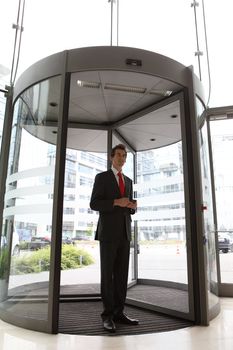 young caucasian businessman at office revolving door with cellphone