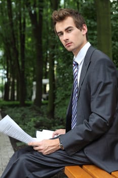 young caucasian businessman in park looking at the documents in his hand