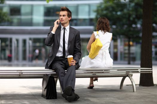 young caucasian businessman sitting on bench using his phone