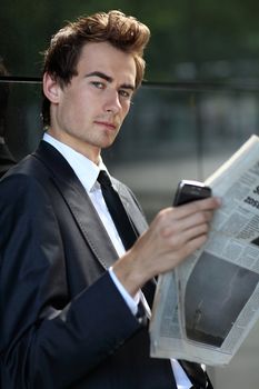 young caucasian businessman standing against the wall and reading