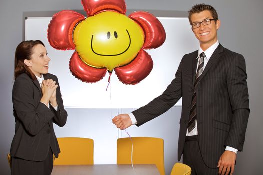 Businessman holding balloon in office while businesswoman smiling
