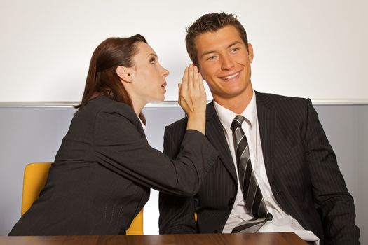 Businesswoman whispering in businessman's ear at office