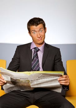 Businessman making face while reading newspaper