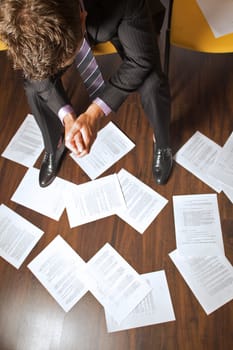 Businessman with clasped hands looking at documents scattered on floor
