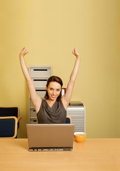 Portrait of businesswoman with arms raised, cup and laptop on desk