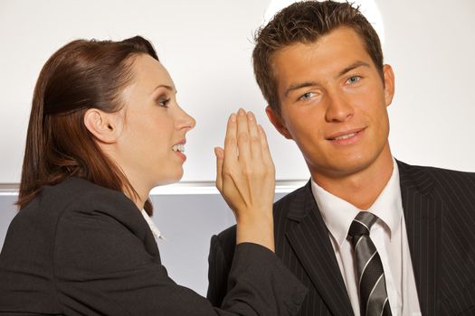 Businesswoman whispering in businessman's ear at office