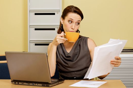 Businesswoman having tea while looking at documents in office