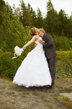The groom passionately kisses the bride among a grass and trees