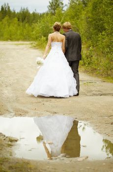 Newly-married couple walks on rural road after a rain