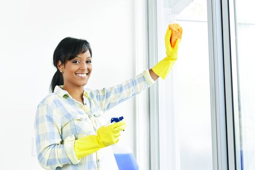 Smiling black woman cleaning windows with glass cleaner