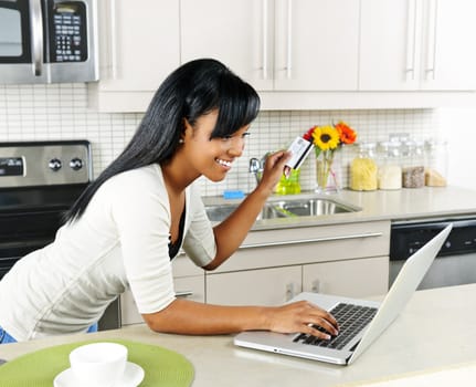 Smiling black woman online shopping using computer and credit card in kitchen