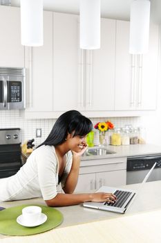 Smiling black woman using computer in modern kitchen interior